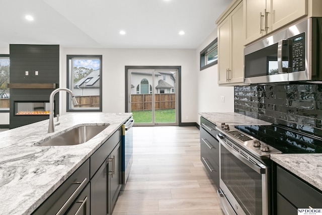 kitchen with stainless steel appliances, light hardwood / wood-style floors, sink, light stone countertops, and cream cabinetry