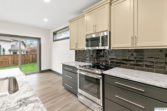 kitchen with cream cabinets, light stone counters, light hardwood / wood-style flooring, tasteful backsplash, and appliances with stainless steel finishes