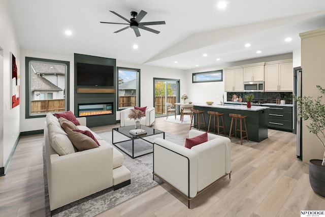 living room with a fireplace, sink, vaulted ceiling, light hardwood / wood-style floors, and ceiling fan