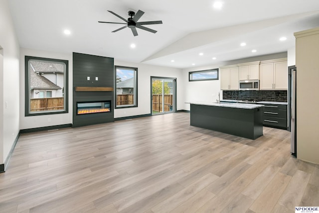 kitchen with vaulted ceiling, light hardwood / wood-style flooring, an island with sink, a fireplace, and appliances with stainless steel finishes