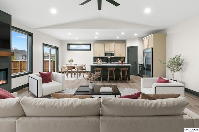 living room with ceiling fan, sink, light hardwood / wood-style flooring, and lofted ceiling