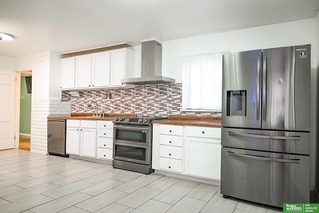 kitchen with butcher block countertops, wall chimney range hood, appliances with stainless steel finishes, and white cabinetry