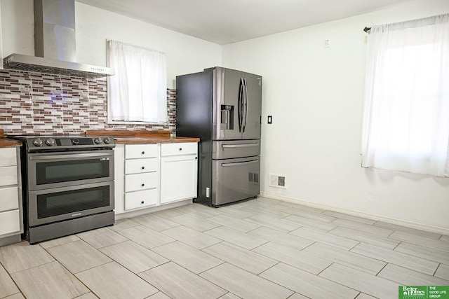 kitchen with stainless steel appliances, white cabinets, wall chimney exhaust hood, tasteful backsplash, and butcher block countertops