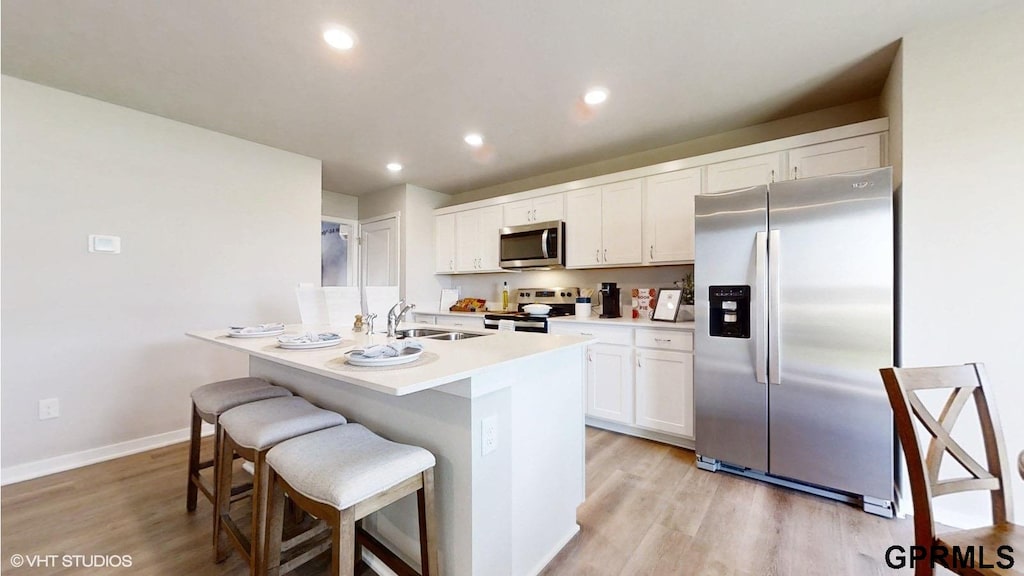 kitchen featuring stainless steel appliances, light wood-type flooring, an island with sink, a breakfast bar, and white cabinets