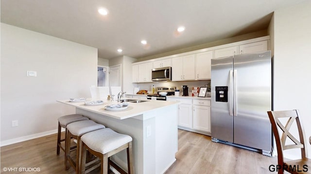 kitchen featuring stainless steel appliances, light wood-type flooring, an island with sink, a breakfast bar, and white cabinets