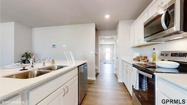 kitchen with stainless steel appliances, light hardwood / wood-style floors, sink, light stone counters, and white cabinets