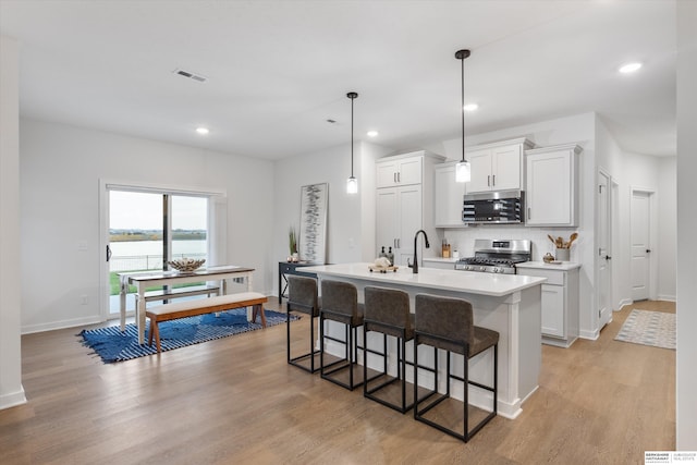 kitchen with stainless steel appliances, an island with sink, decorative light fixtures, and light hardwood / wood-style flooring