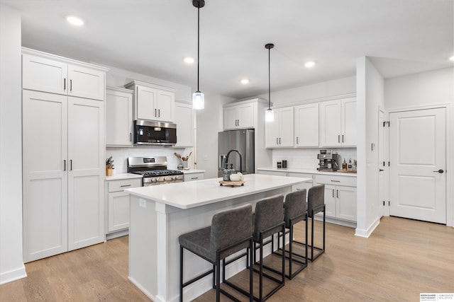 kitchen with a center island with sink, a breakfast bar, appliances with stainless steel finishes, white cabinets, and pendant lighting