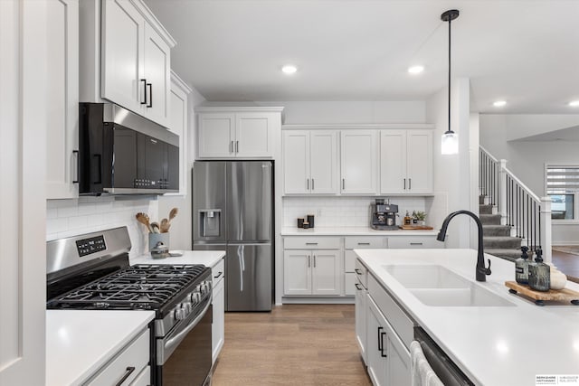 kitchen featuring stainless steel appliances, white cabinetry, pendant lighting, sink, and light hardwood / wood-style floors