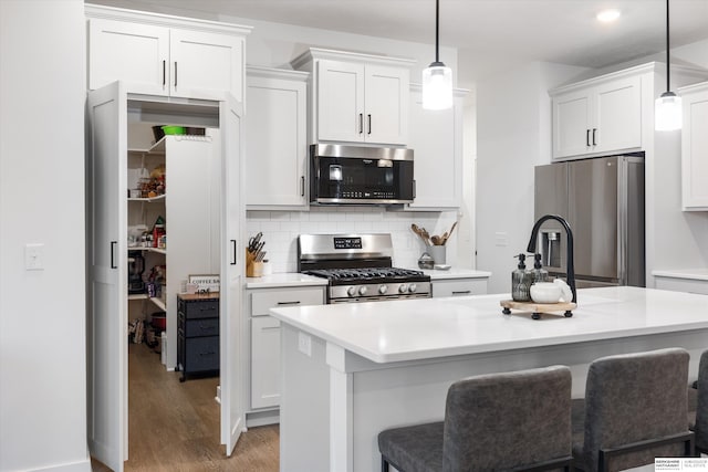 kitchen featuring a kitchen island with sink, wood-type flooring, decorative light fixtures, and appliances with stainless steel finishes