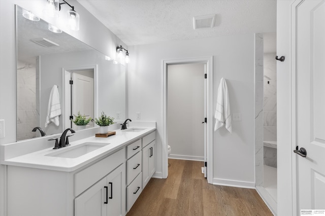 bathroom featuring hardwood / wood-style flooring, a textured ceiling, vanity, tiled shower, and toilet