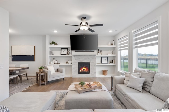 living room with a stone fireplace, hardwood / wood-style flooring, and ceiling fan