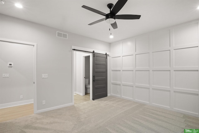 unfurnished bedroom featuring a barn door, light carpet, ceiling fan, and ensuite bath