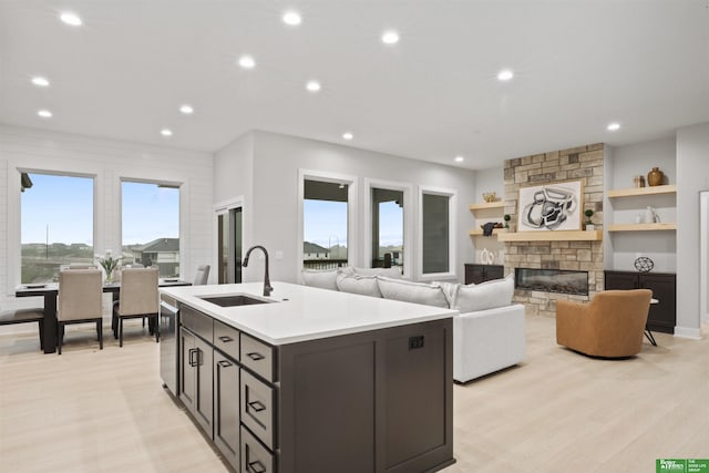 kitchen featuring a fireplace, dark brown cabinetry, sink, an island with sink, and light hardwood / wood-style floors