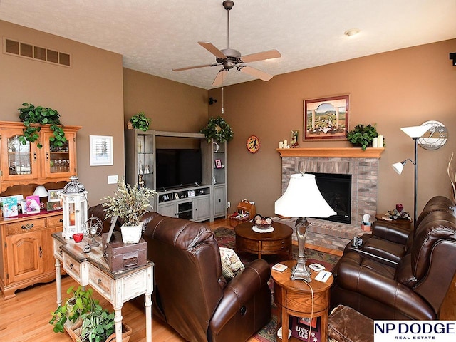 living room featuring light wood-type flooring, ceiling fan, and a fireplace