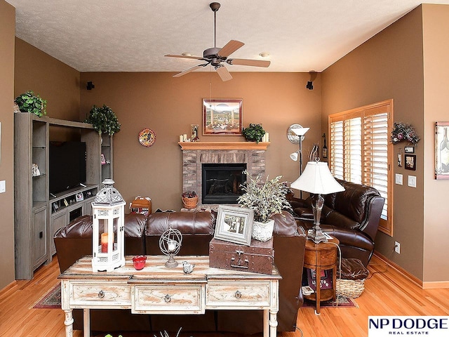 living room featuring ceiling fan, light hardwood / wood-style floors, a stone fireplace, and a textured ceiling