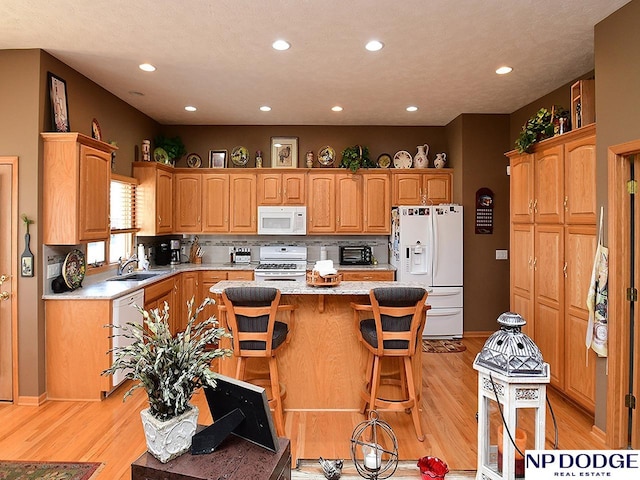 kitchen with white appliances, a kitchen bar, light hardwood / wood-style flooring, and a kitchen island