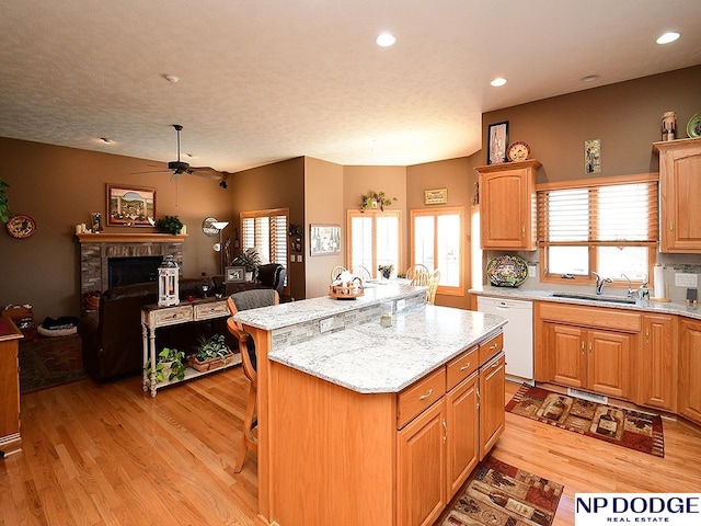 kitchen with a kitchen island, white dishwasher, sink, light hardwood / wood-style floors, and a brick fireplace