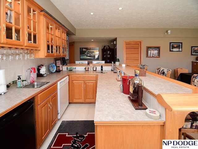 kitchen with a textured ceiling, white dishwasher, sink, dishwasher, and kitchen peninsula