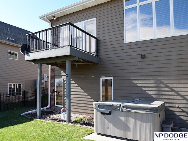 rear view of property with a hot tub, a lawn, and a balcony