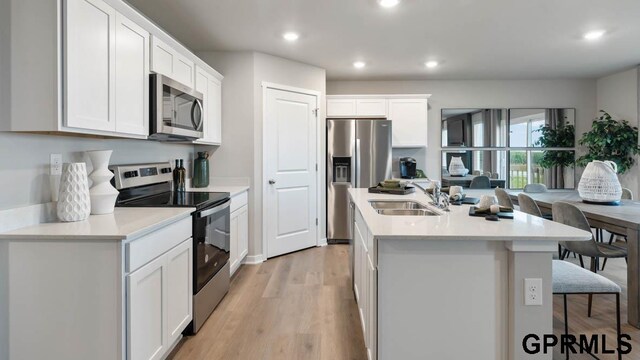 kitchen with stainless steel appliances, white cabinetry, sink, and a kitchen island with sink