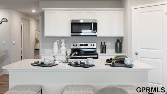 kitchen featuring stainless steel appliances, white cabinets, hardwood / wood-style flooring, an island with sink, and a kitchen breakfast bar