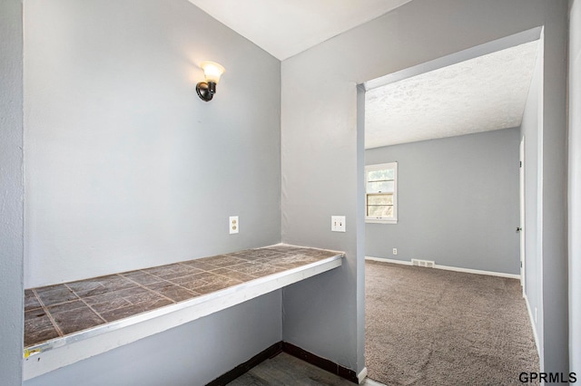 hallway with dark colored carpet and a textured ceiling