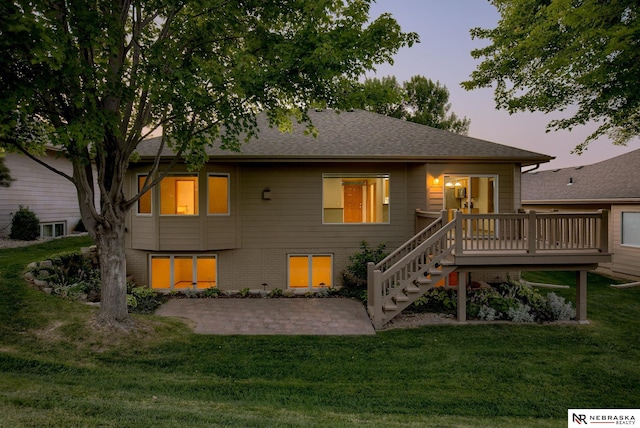 back house at dusk with a deck, a yard, and a patio