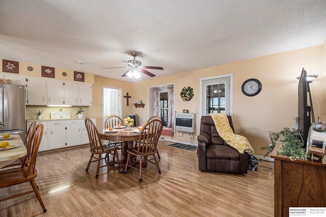 dining space with heating unit, ceiling fan, light hardwood / wood-style floors, and a textured ceiling