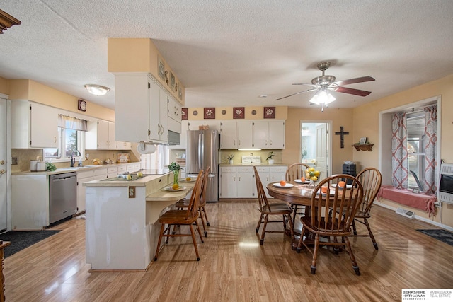 interior space with light wood-type flooring, a textured ceiling, heating unit, ceiling fan, and sink