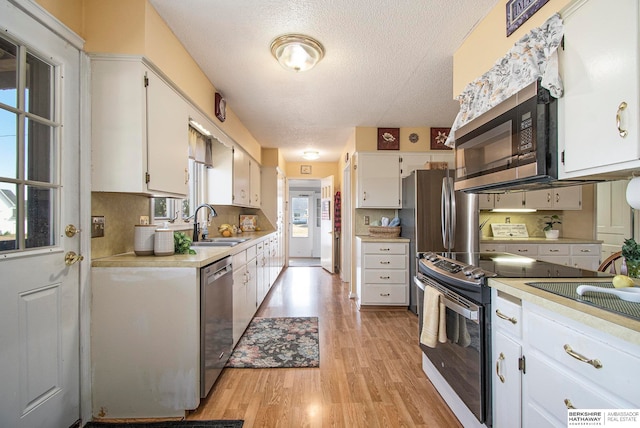 kitchen with sink, appliances with stainless steel finishes, a textured ceiling, white cabinets, and light wood-type flooring