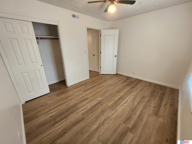 unfurnished bedroom featuring ceiling fan, a textured ceiling, a closet, and wood-type flooring