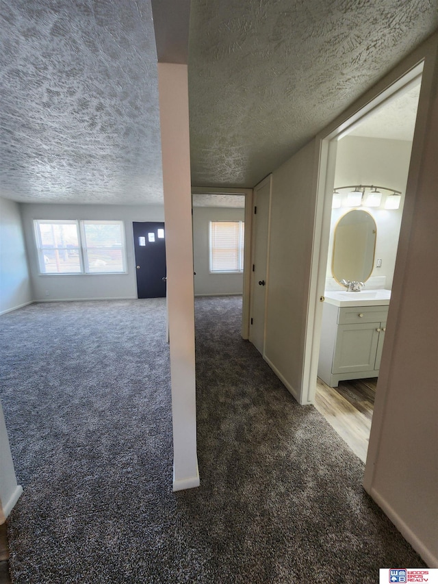 unfurnished living room featuring dark colored carpet, a textured ceiling, and sink