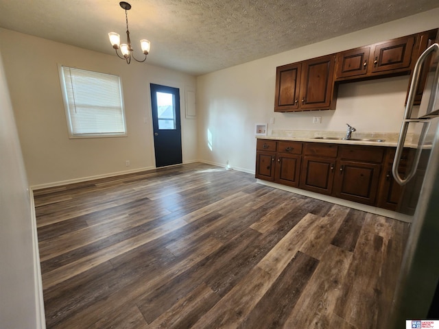 kitchen featuring stainless steel refrigerator, dark brown cabinets, dark hardwood / wood-style floors, hanging light fixtures, and sink