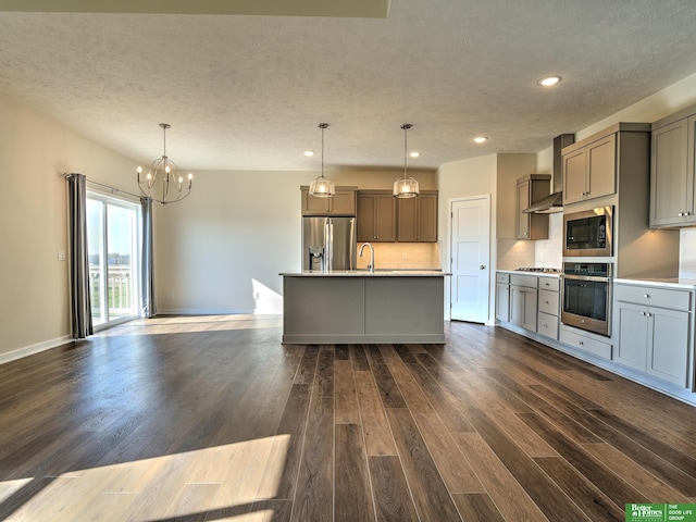 kitchen with dark wood-type flooring, a kitchen island with sink, pendant lighting, and appliances with stainless steel finishes