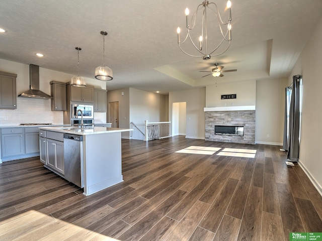 kitchen featuring a center island with sink, appliances with stainless steel finishes, dark hardwood / wood-style floors, wall chimney range hood, and pendant lighting