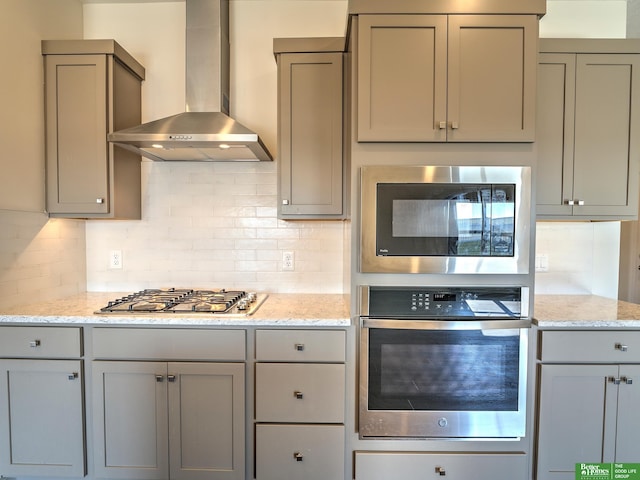 kitchen featuring light stone counters, backsplash, appliances with stainless steel finishes, and wall chimney exhaust hood