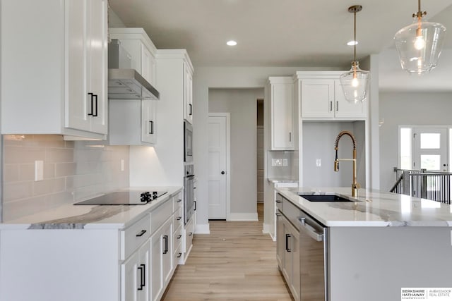 kitchen with stainless steel appliances, wall chimney range hood, hanging light fixtures, sink, and white cabinets