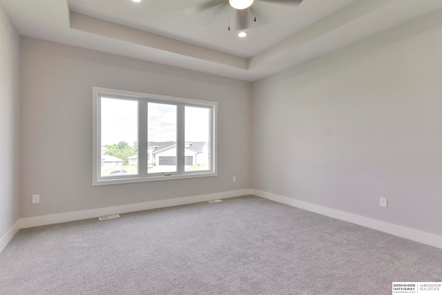 carpeted empty room featuring ceiling fan and a raised ceiling