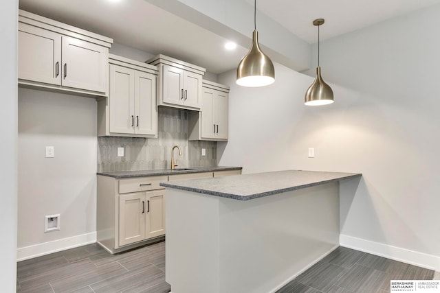 kitchen featuring sink, kitchen peninsula, backsplash, white cabinets, and pendant lighting