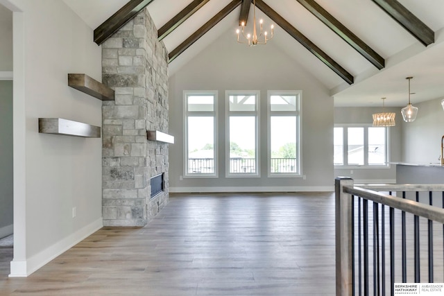 unfurnished living room featuring a fireplace, beam ceiling, high vaulted ceiling, light hardwood / wood-style floors, and a chandelier