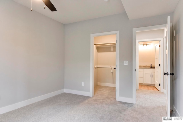 unfurnished bedroom with light colored carpet, sink, ceiling fan, a closet, and a walk in closet