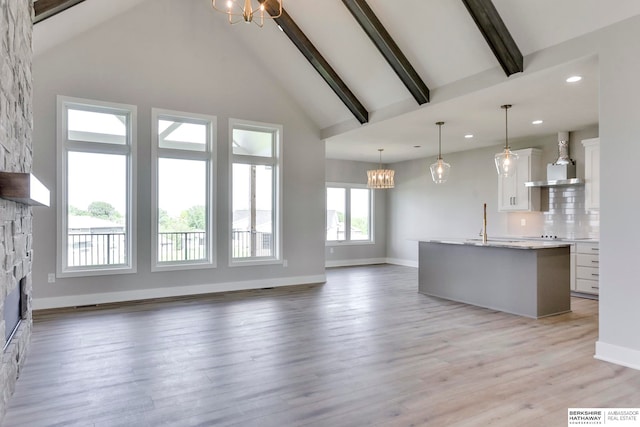 unfurnished living room featuring high vaulted ceiling, light hardwood / wood-style floors, beam ceiling, and an inviting chandelier