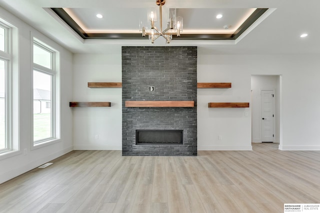 unfurnished living room with a stone fireplace, a wealth of natural light, a raised ceiling, and light hardwood / wood-style flooring