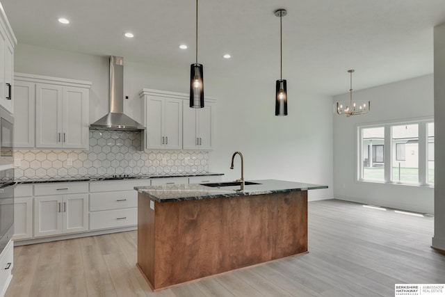 kitchen featuring white cabinets, sink, wall chimney range hood, pendant lighting, and light wood-type flooring