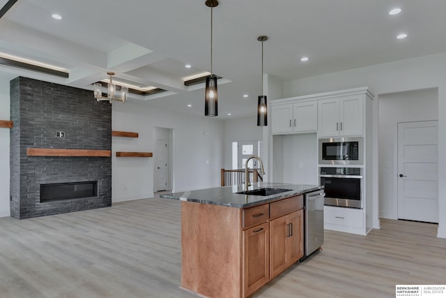 kitchen with stainless steel appliances, white cabinetry, sink, light hardwood / wood-style floors, and a kitchen island with sink