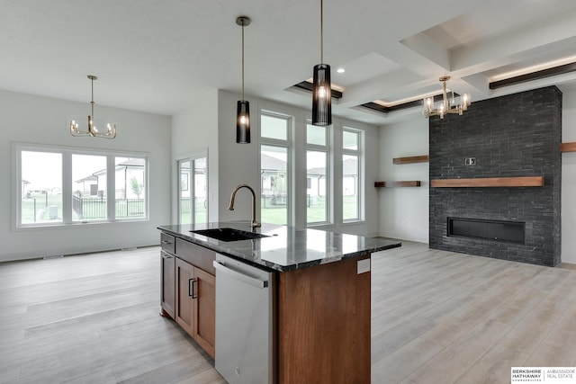 kitchen featuring light hardwood / wood-style floors, dark stone counters, dishwasher, sink, and a fireplace