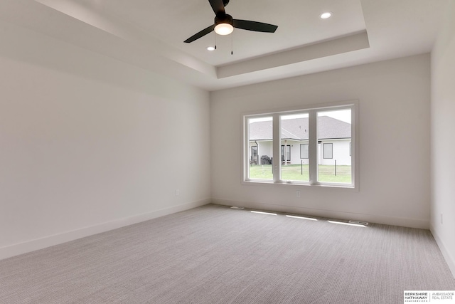 carpeted empty room with ceiling fan and a raised ceiling