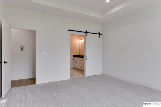 unfurnished bedroom with connected bathroom, a barn door, and light carpet