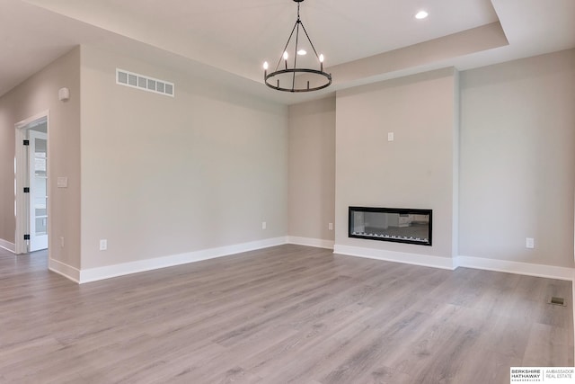 unfurnished living room featuring a chandelier and light hardwood / wood-style floors